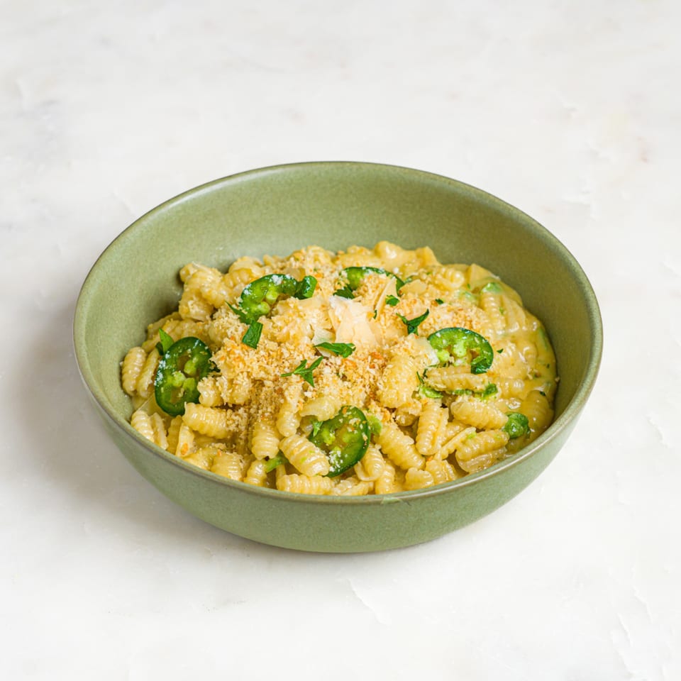 A'mano's cavatappi pasta with creamy sauce, topped with jalapeños, breadcrumbs, and fresh herbs in a green bowl.