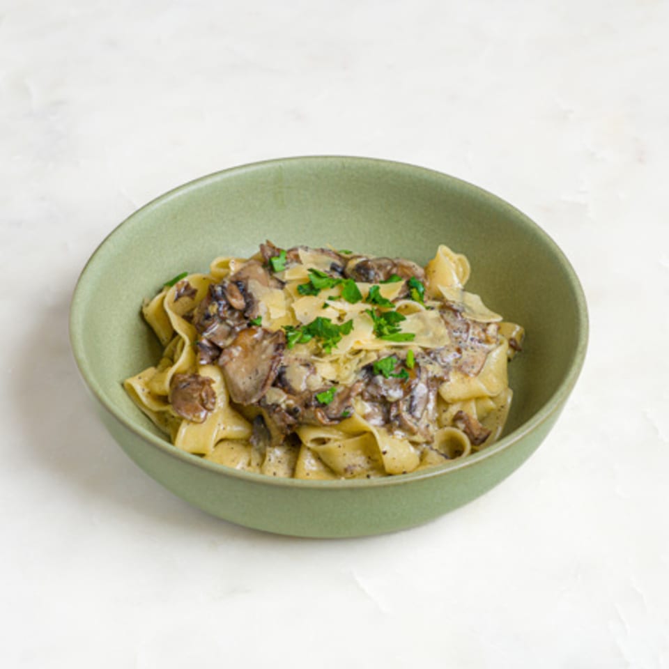 A'mano Fresh Pasta Kitchen's pappardelle pasta with creamy mushroom sauce, parmesan, and parsley in a green bowl.
