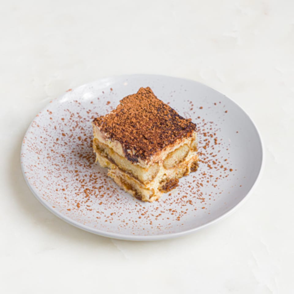 A'mano Fresh Pasta Kitchen's tiramisu dessert, dusted with cocoa powder, on a white plate.