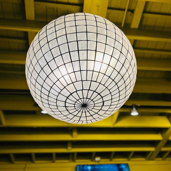 A large, spherical, capiz shell chandelier hangs from a bright yellow ceiling at A'mano Fresh Pasta Kitchen.