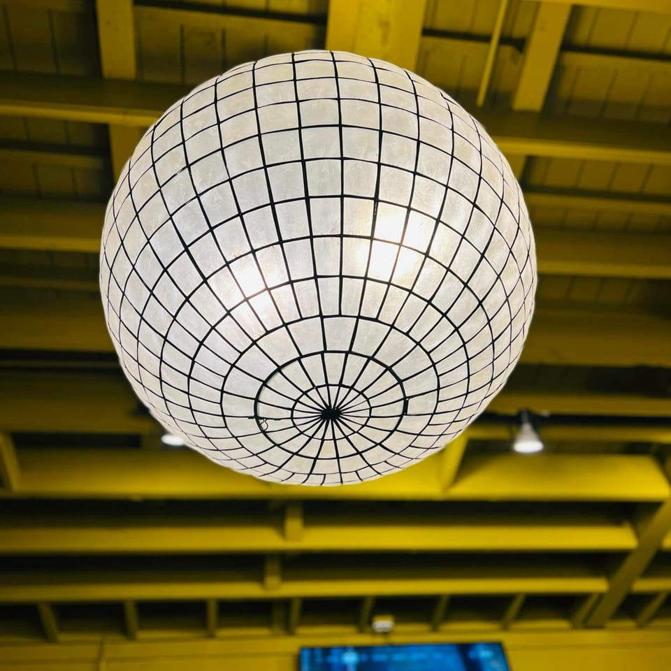 A large, spherical, capiz shell chandelier hangs from a bright yellow ceiling at A'mano Fresh Pasta Kitchen.