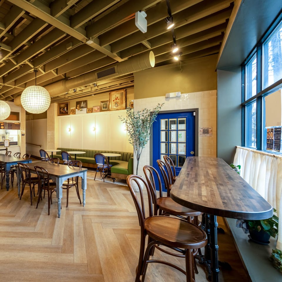 Interior of A'mano Fresh Pasta Kitchen with dining tables, green banquette seating, and a blue door.