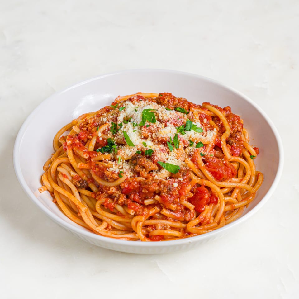 A'mano Fresh Pasta Kitchen's bucatini pasta with bolognese sauce, parmesan, and fresh parsley in a white bowl.