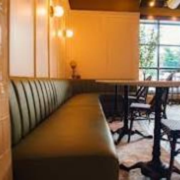 A'mano Fresh Pasta Kitchen interior with a long brown booth, tables, chairs, and a large window.
