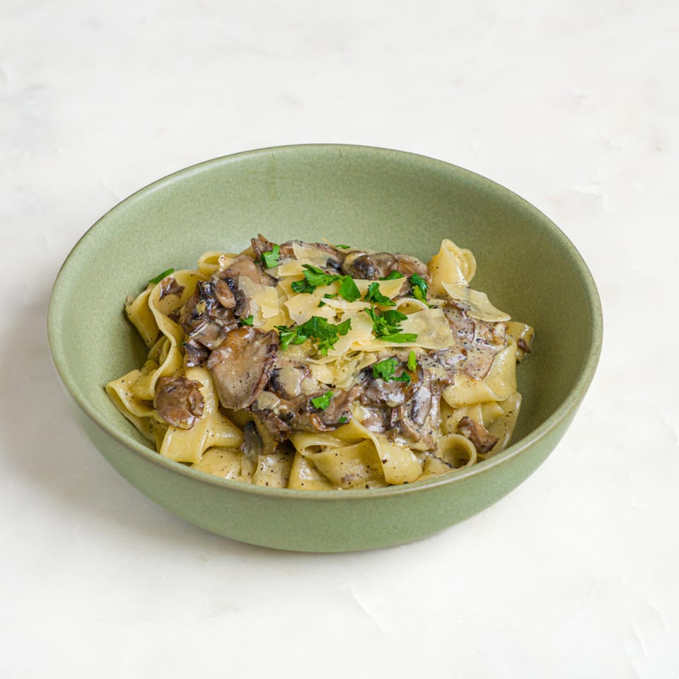 A'mano Fresh Pasta Kitchen's pappardelle with creamy mushroom sauce, parmesan, and fresh parsley in a green bowl.