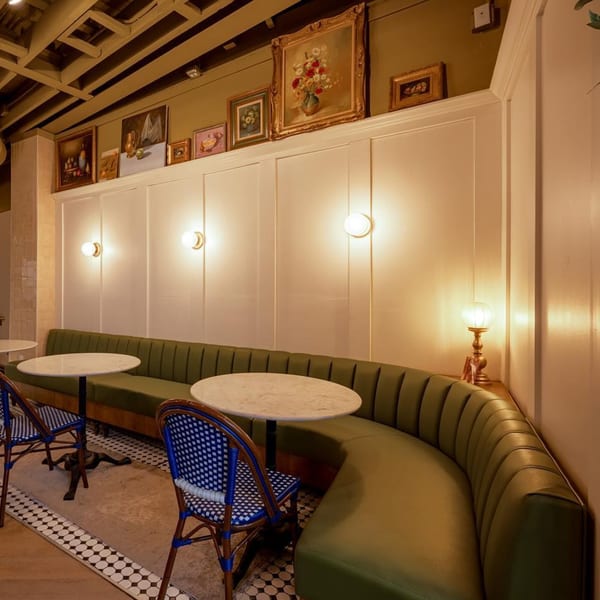 A'mano Fresh Pasta Kitchen's interior with green banquette seating, marble tables, and framed art on the wall.