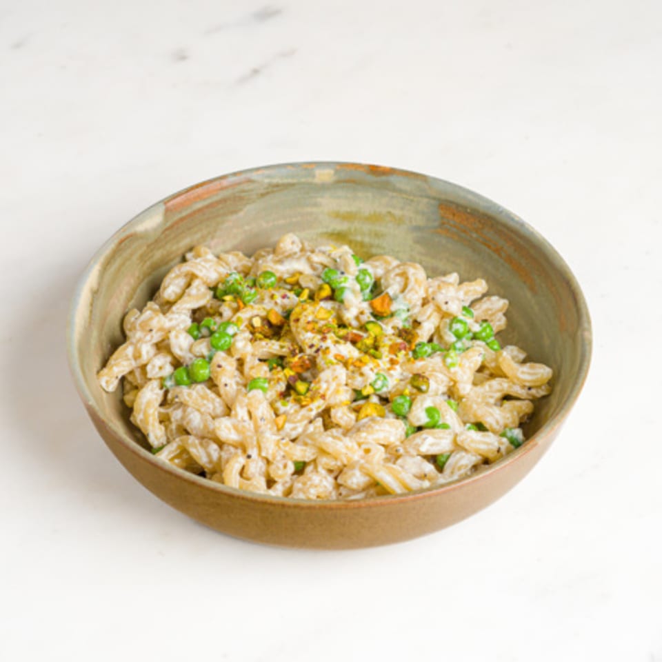 A'mano Fresh Pasta Kitchen's creamy pasta with green peas and pistachios in a rustic bowl.