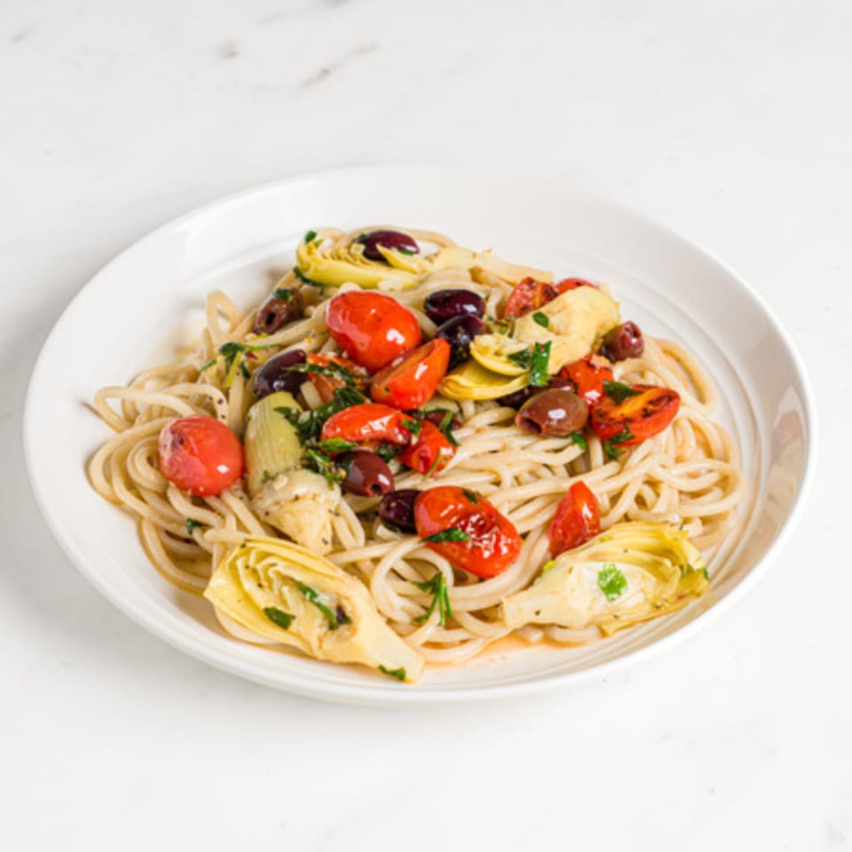 A'mano Fresh Pasta Kitchen's spaghetti with cherry tomatoes, olives, and artichoke hearts in a white bowl.