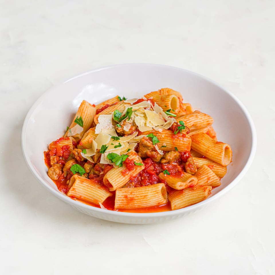 A'mano Fresh Pasta Kitchen's rigatoni with sausage ragu, parmesan, and parsley in a white bowl.